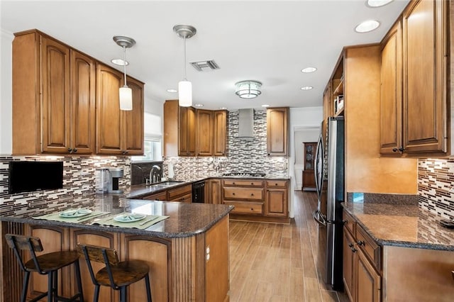 kitchen featuring appliances with stainless steel finishes, wall chimney range hood, hanging light fixtures, light hardwood / wood-style floors, and tasteful backsplash