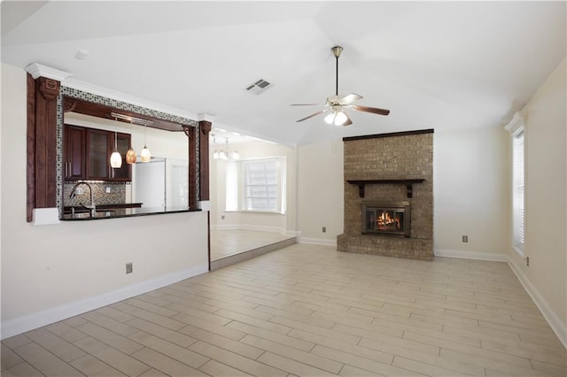 unfurnished living room with ceiling fan with notable chandelier, a fireplace, brick wall, and vaulted ceiling