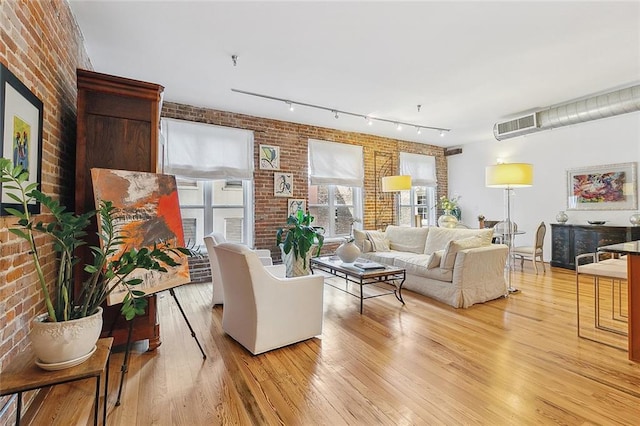 living room featuring track lighting, light hardwood / wood-style flooring, and brick wall