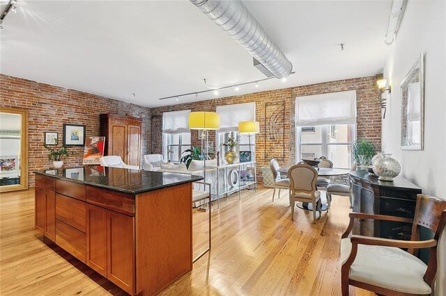 kitchen with light wood-type flooring, track lighting, a center island, dark stone counters, and brick wall