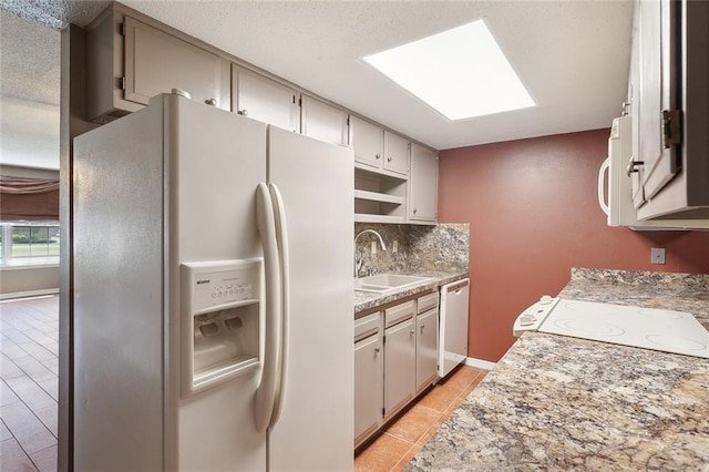 kitchen featuring a skylight, white appliances, sink, tasteful backsplash, and light tile patterned flooring