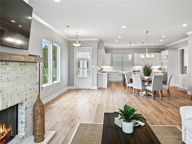 living room featuring ornamental molding, a notable chandelier, a fireplace, and light hardwood / wood-style flooring