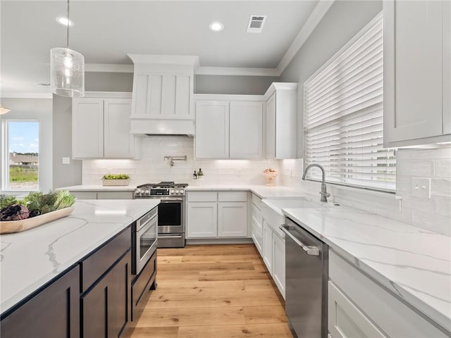 kitchen with sink, white cabinetry, crown molding, appliances with stainless steel finishes, and pendant lighting