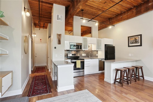 kitchen with appliances with stainless steel finishes, white cabinets, track lighting, and wood ceiling