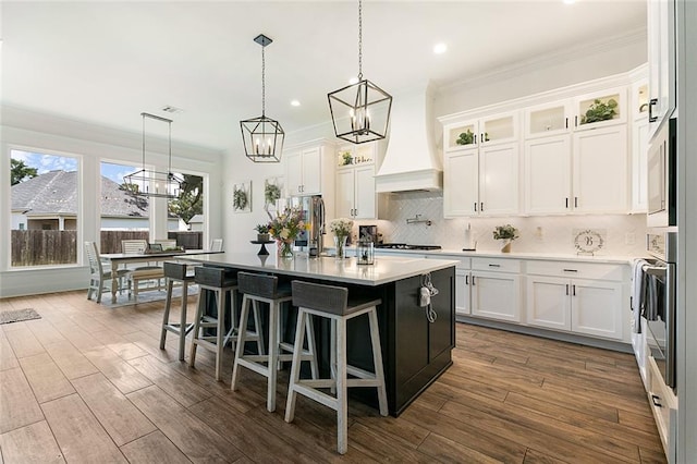 kitchen with backsplash, white cabinets, an island with sink, and hanging light fixtures