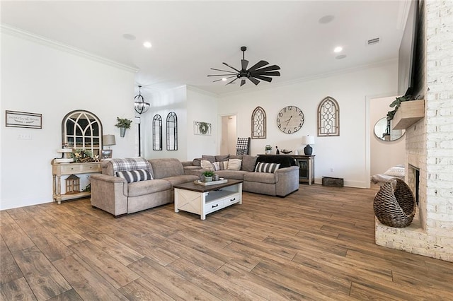 living room with wood-type flooring, a stone fireplace, and crown molding