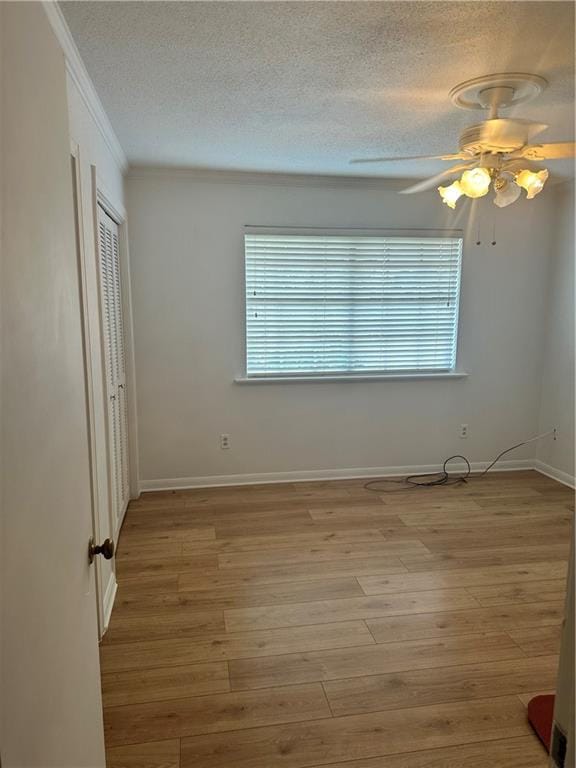 empty room with a textured ceiling, crown molding, ceiling fan, and light hardwood / wood-style floors