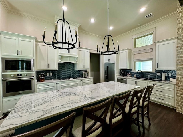 kitchen with appliances with stainless steel finishes, dark wood-type flooring, tasteful backsplash, exhaust hood, and hanging light fixtures