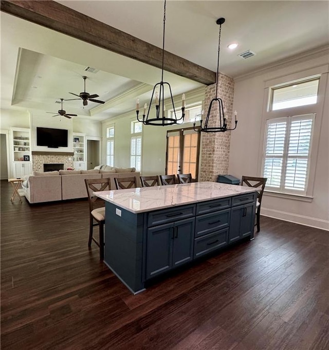 kitchen featuring built in features, dark wood-type flooring, ceiling fan with notable chandelier, light stone countertops, and a fireplace