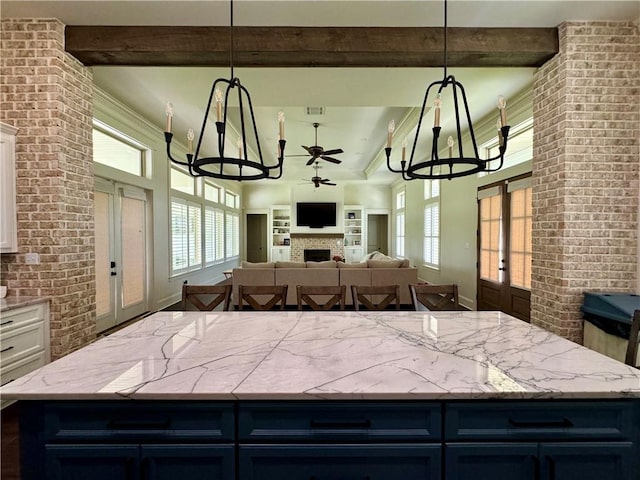 kitchen with ceiling fan with notable chandelier, brick wall, and white cabinets