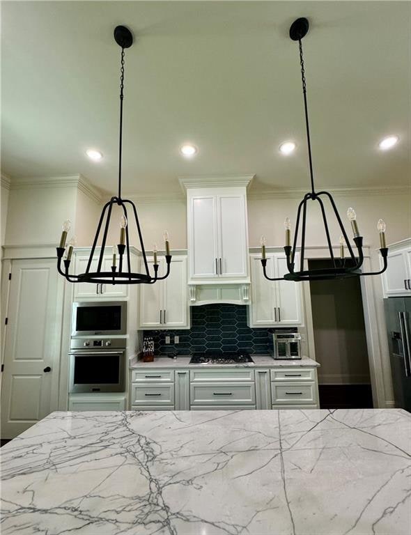 kitchen featuring stainless steel appliances, decorative backsplash, white cabinetry, light stone counters, and pendant lighting