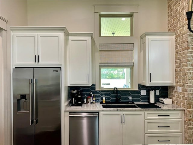 kitchen featuring stainless steel appliances, sink, brick wall, light stone counters, and white cabinets