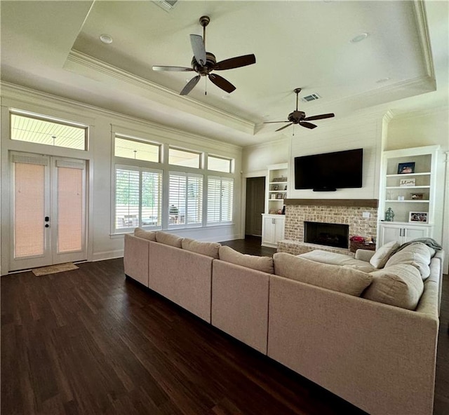 living room with french doors, dark hardwood / wood-style floors, a raised ceiling, ceiling fan, and a brick fireplace