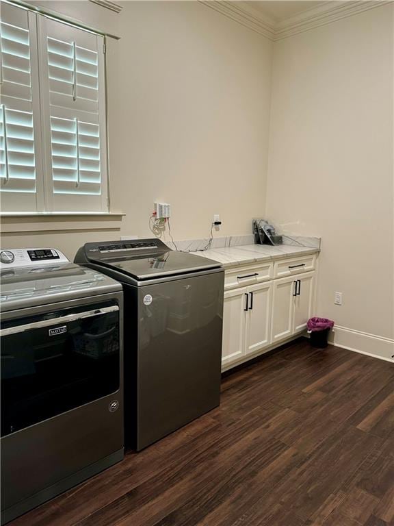 clothes washing area with washing machine and dryer, dark hardwood / wood-style flooring, crown molding, and cabinets