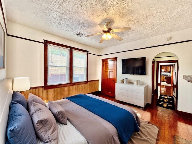 bedroom featuring a textured ceiling, dark wood-type flooring, wood walls, and ceiling fan