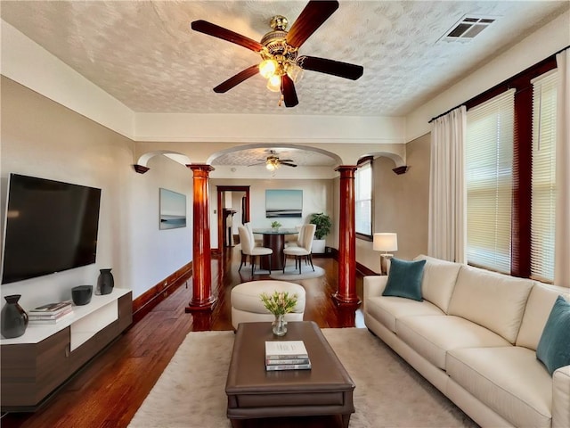 living room featuring ceiling fan, dark wood-type flooring, decorative columns, and a textured ceiling