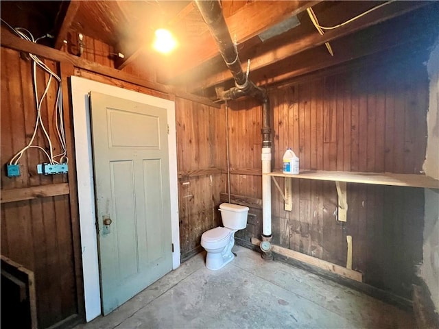 bathroom with toilet, concrete flooring, and wood walls