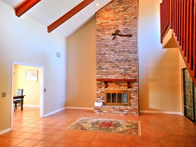 unfurnished living room with tile patterned flooring, beam ceiling, high vaulted ceiling, and brick wall