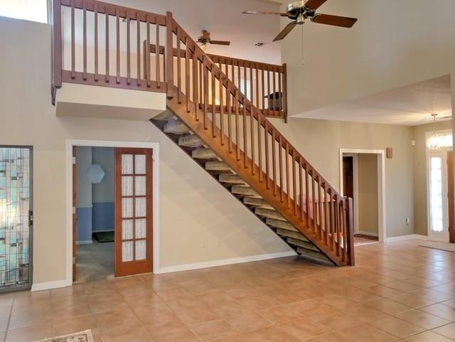 staircase with ceiling fan with notable chandelier, a high ceiling, and tile patterned flooring