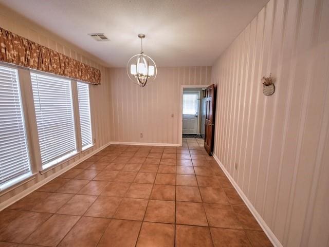 tiled spare room featuring a notable chandelier