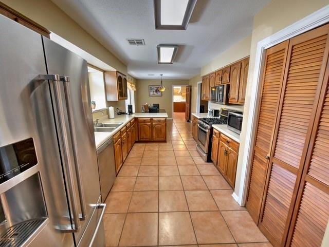 kitchen featuring sink, appliances with stainless steel finishes, light tile patterned floors, kitchen peninsula, and pendant lighting