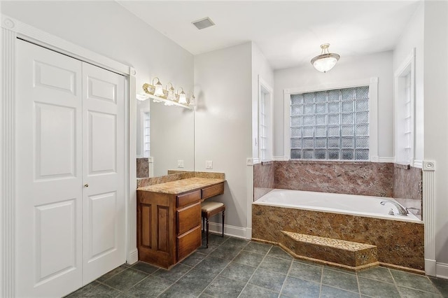 bathroom with tile patterned flooring, vanity, and a relaxing tiled tub