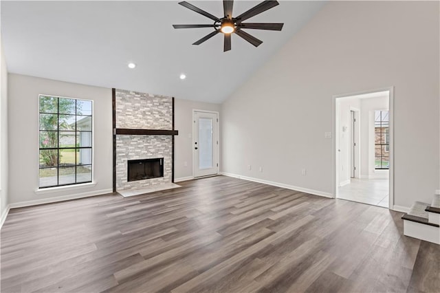 unfurnished living room with ceiling fan, a stone fireplace, high vaulted ceiling, and wood-type flooring