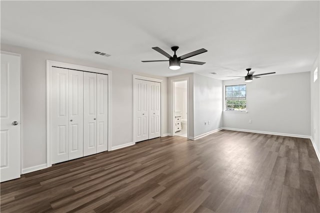 unfurnished bedroom featuring ceiling fan, dark wood-type flooring, two closets, and ensuite bathroom