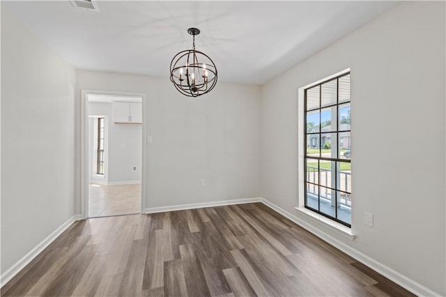 spare room featuring wood-type flooring, plenty of natural light, and a chandelier