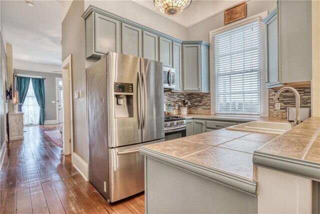 kitchen with tasteful backsplash, hardwood / wood-style floors, tile countertops, sink, and stainless steel appliances