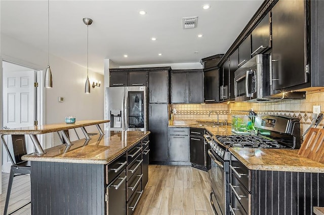 kitchen with appliances with stainless steel finishes, decorative light fixtures, backsplash, a kitchen bar, and light stone counters