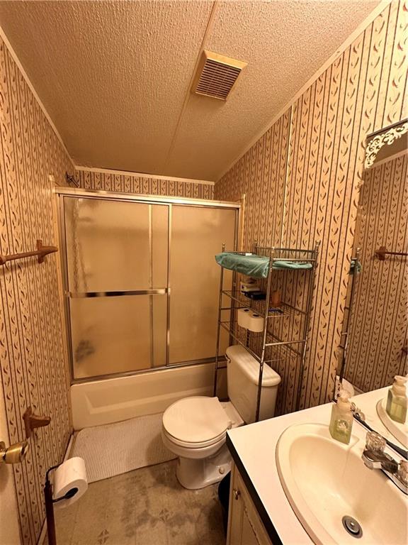 full bathroom featuring toilet, a textured ceiling, and shower / bath combination with glass door