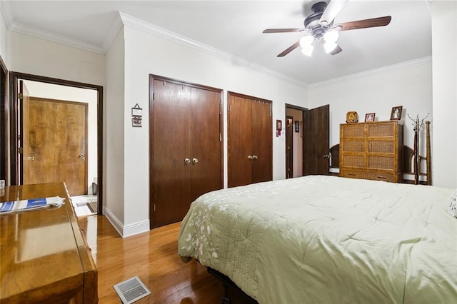 bedroom featuring baseboards, visible vents, ornamental molding, wood finished floors, and multiple closets