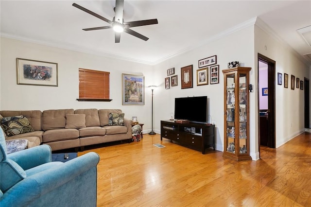 living area featuring light wood finished floors, attic access, baseboards, ceiling fan, and crown molding