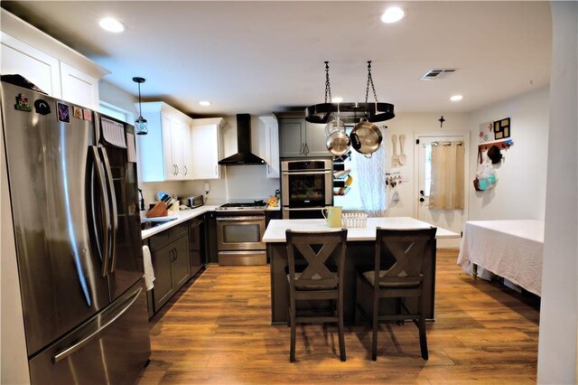 kitchen featuring light wood-type flooring, appliances with stainless steel finishes, a kitchen island, wall chimney range hood, and white cabinets