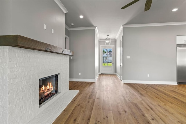 unfurnished living room featuring ornamental molding, hardwood / wood-style floors, ceiling fan with notable chandelier, and a fireplace