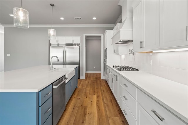 kitchen featuring stainless steel appliances, premium range hood, a center island with sink, white cabinets, and light hardwood / wood-style floors