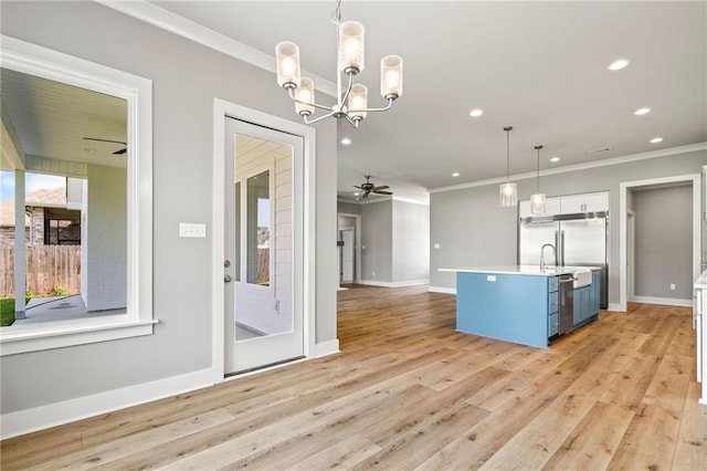 kitchen with a kitchen island with sink, pendant lighting, light wood-type flooring, ceiling fan with notable chandelier, and blue cabinets