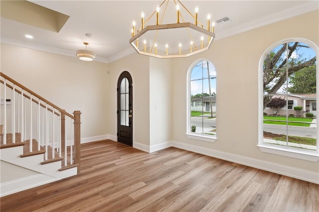 foyer entrance featuring light wood-type flooring, crown molding, and a notable chandelier