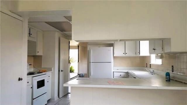 kitchen with light tile patterned floors, white appliances, white cabinetry, sink, and kitchen peninsula