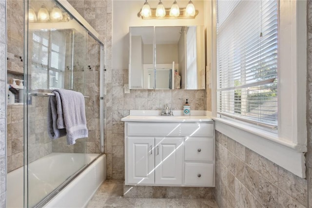 bathroom featuring tile patterned flooring, tile walls, vanity, and enclosed tub / shower combo