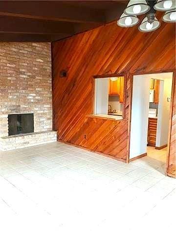 8002 Trapier Ave, New Orleans, LA 70127 - unfurnished living room featuring a brick fireplace, wooden walls, and vaulted ceiling with beams
