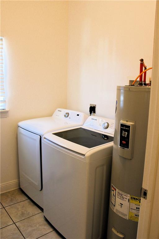 clothes washing area with washer and dryer, light tile patterned floors, and water heater