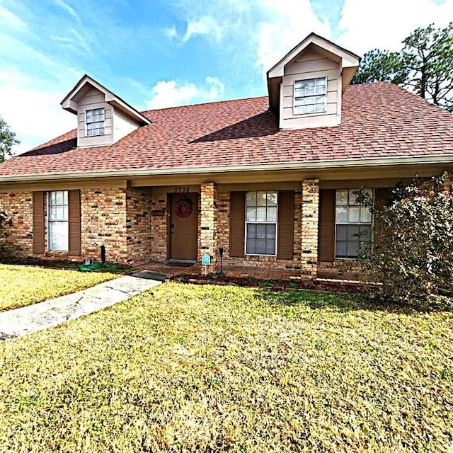 view of front of house with a front yard, brick siding, and a shingled roof