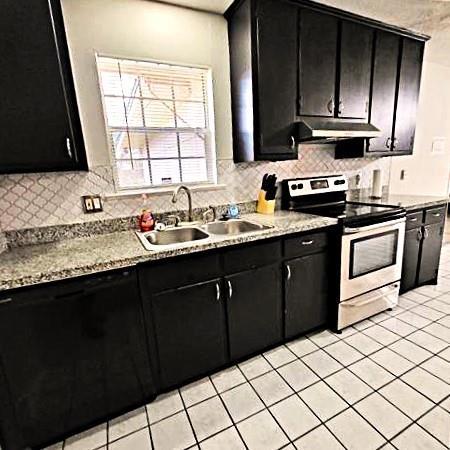 kitchen with decorative backsplash, sink, light tile patterned flooring, and stainless steel range with electric stovetop