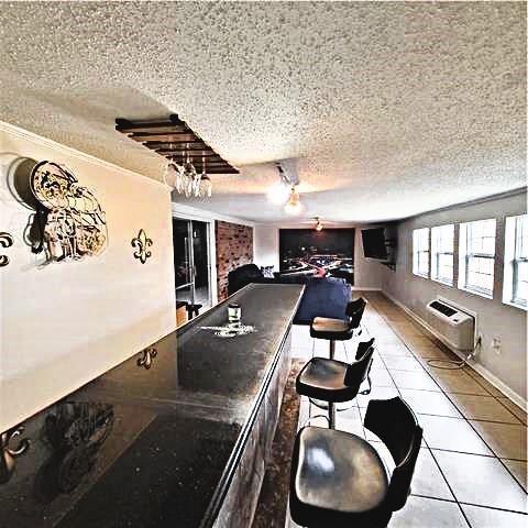 rec room with crown molding, a textured ceiling, an AC wall unit, and light tile patterned floors