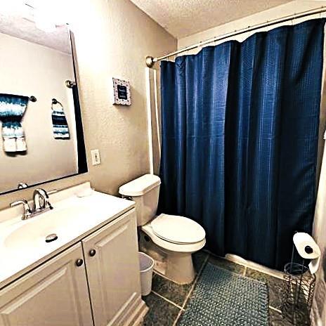 bathroom featuring a textured ceiling, vanity, curtained shower, tile patterned flooring, and toilet