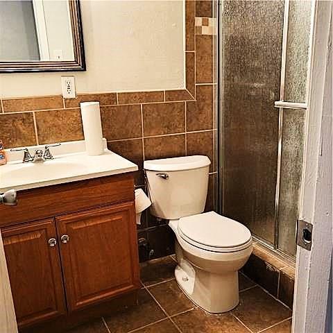 bathroom with toilet, walk in shower, tile patterned flooring, vanity, and tile walls