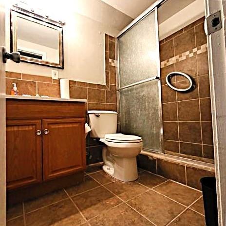 bathroom with a shower with door, vanity, tile patterned flooring, tile walls, and toilet