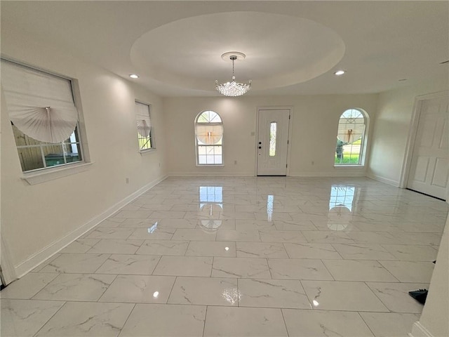 empty room featuring plenty of natural light, a raised ceiling, and an inviting chandelier